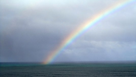 Dunkle Meeroberfläche, auf die ein Regenbogen von rechts oben fällt.