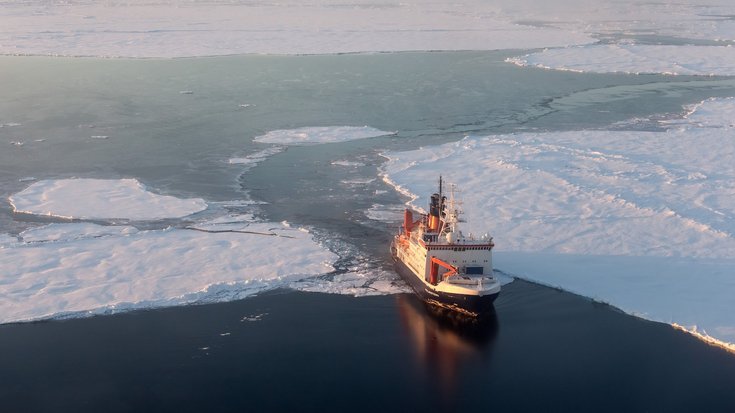 Das Foto zeigt ein Schiff auf einem teils zugefrorenen Ozean aus der Vogelperspektive.