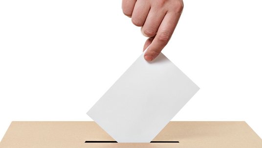 Hand wirft Briefumschlag in Wahlurne