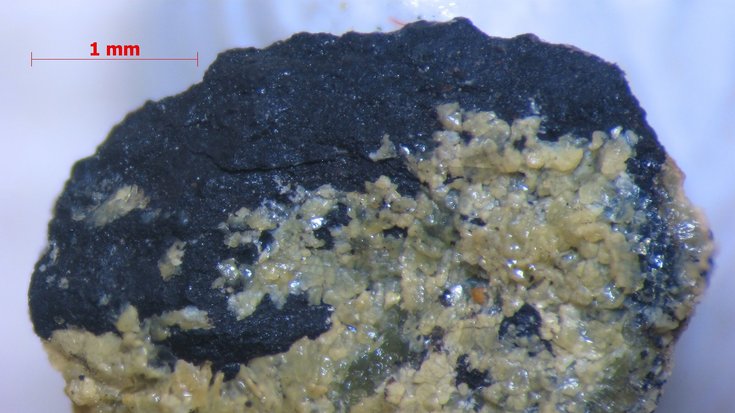 Schwarzer Stein, der auf einer Seite von einem hellen Mineral überzogen ist