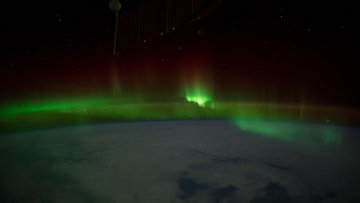 Foto eines Teils der Erdoberfläche aus dem Weltall aufgenommen: In der Atmosphäre breitet sich ein grüner Schimmer aus.