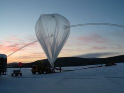 Foto, ein transparenter, fast haushoher Ballon, der in den Himmel ragt. Er ist am schneebedeckten Boden befestigt. Im Hintergrund eine flache Landschaft.
