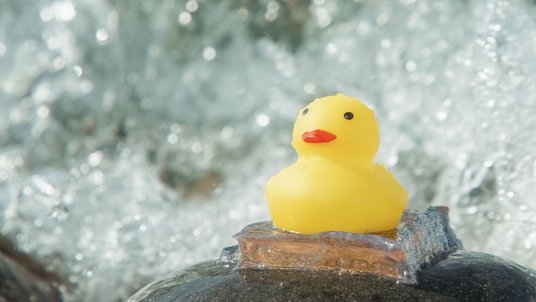 Eine gelbe Ente klebt auf einem Stein, im Hintergrund fließendes Wasser