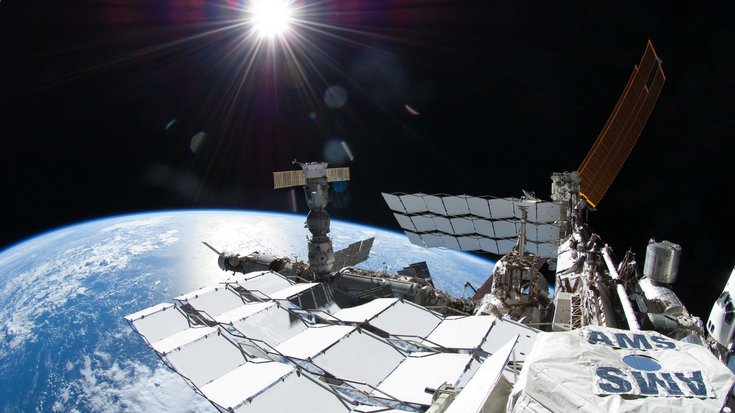 Raumstation vor der Erde, im Vordergrund ein mit "AMS" beschriftetes Bauteil.