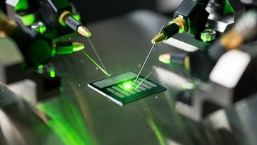 Auf einer Glasplatte liegt ein Mikrochip und wird mit Laserlicht bestrahlt.