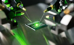 Auf einer Glasplatte liegt ein Mikrochip und wird mit Laserlicht bestrahlt.