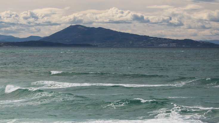 Atlantischer Ozean an französischer Küste Meeresküste vor einem Berg. Darüber wolkenverhangener Himmel.