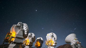 Vier Parabol-Radioantennen vor dem südlichen Nachthimmel. Im Hintergrund ein Gebirgszug.