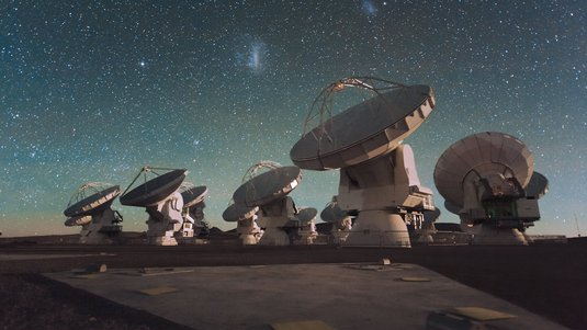 Mehrere weiße Teleskopschüsseln unter einem Sternhimmel