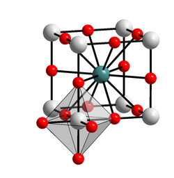 Grafik: Würfel, an dessen Ecken graue Kugeln sitzen (Barium), an den Kanten dazwischen kleinere rote Kugeln (Sauerstoff), im Raumzentrum des Würfels eine türkise Kugel (Titan). Am vorderen linken unteren Eck ist noch ein Oktaeder angefügt, mit dem Würfeleck als Zentrum und sechs roten Kugeln Sauerstoff, je eine in jeder Raumrichtung.