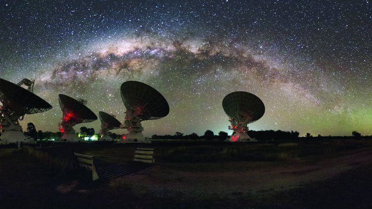 Mehrere Radioteleskope unter Sternenhimmel mit Milchstraße.
