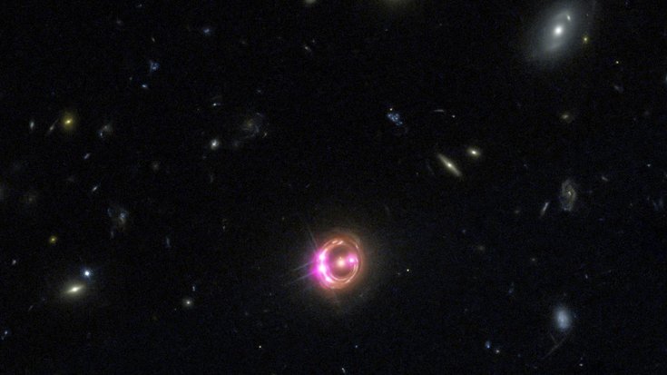 Viele Galaxien, die Galaxie in der Bildmitte ist von einem Ring umgeben, in dem sich vier helle Strahlungsquellen befinden.