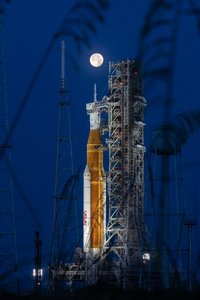 Die Rakete steht auf der Erde. Im Hintergrund ist der Mond am Himmel abgebildet.