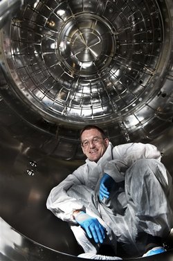 Foto. Mann im weißen Schutzanzug mit blauen Handschuhen in einer metallischen Kammer.