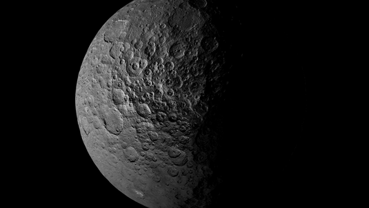 Das Bild zeigt Ceres, der zur Hälfte von Licht beschienen ist. Auf der Oberfläche sind viele Krater zu erkennen.