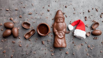 Auf einem Tisch liegen verschiedene Leckereien aus Schokolade, darunter ein Schokoladenweihnachtsmann, sowie eine Weihnachtsmannmütze