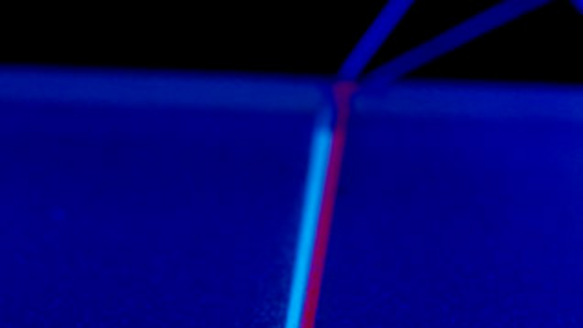 eine rote und eine blaue dünne Leitung laufen nebeneinander durch die Mitte des Bildes. Eine kreisförmige Unterbrechung auf dunklem Hintergrund.