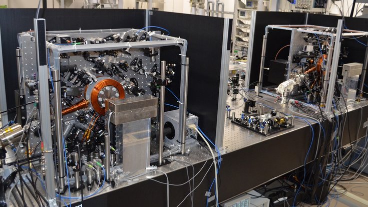 Auf einem Tisch im Labor stehen zwei senkrechte Platten mit vielen Spiegeln und Optiken, die die Atomuhren sind.