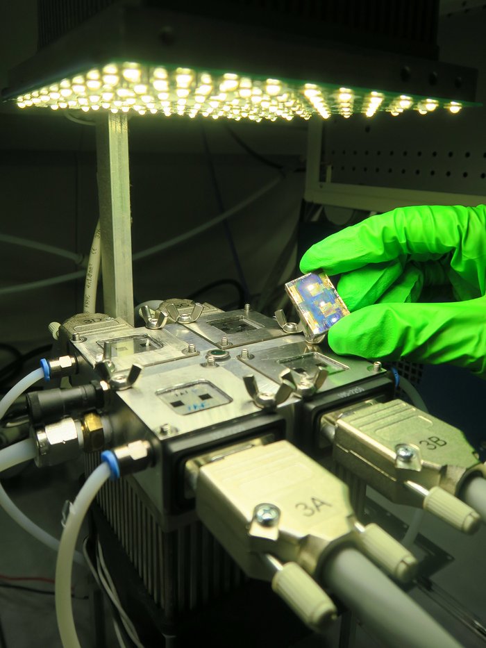 Neuer Teststand simuliert reale Bedingungen Forscher hält Solarzelle in einer Hand mit Schutzhandschuh über eine Apparatur.