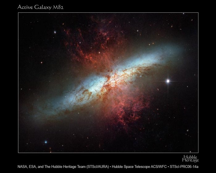 Eine Galaxie von der Seite; die Sternscheibe erscheint unter flachem Winkel; vom Zentrum erstrecken sich rechtwinklig zu beiden Seiten rote Gasfetzen.