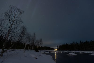 Das Foto zeigt eine verschneite Landschaft in der Nacht. Am Himmel sind diffuse Leuchterscheinungen zu sehen.