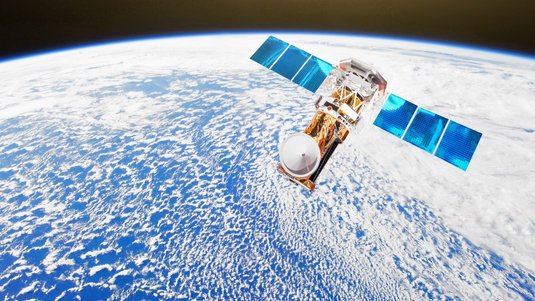 Satellit im All, der an der Erde vorbeifliegt. Im Hintergrund sieht man eine Wolkendecke über dem blauen Planeten.