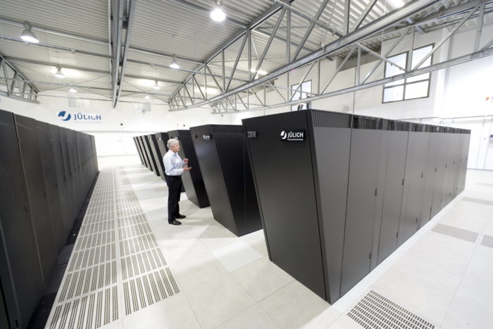 Rechnerhalle des Jülich Supercomputing Centre Mannshohe Computerschränke stehen aufgereiht in einer sonst leeren Halle.