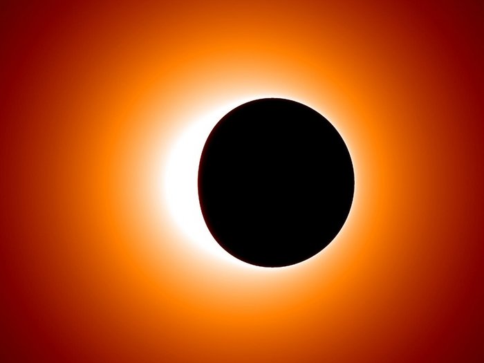 Schatten des Ereignishorizonts in der Simulation Schwarzer, fast kreisförmiger Fleck vor einem hellen Hintergrund in gelb und orange.
