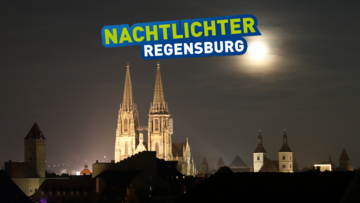 Dächer einer Stadt bei Nacht mit einer angeleuchteten Kirche im Mittelpunkt.