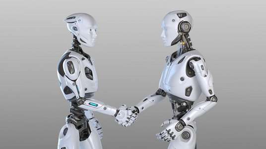 Zwei humanoide, weiß-silberne Roboter mit leuchtend blauen Augen stehen sich seitlich gegenüber und schütteln sich die Hand, vor neutralem hellgrauem Hintergrund. Sichtbare Gelenke und Kabel unterstreichen ihren technischen Aufbau.
