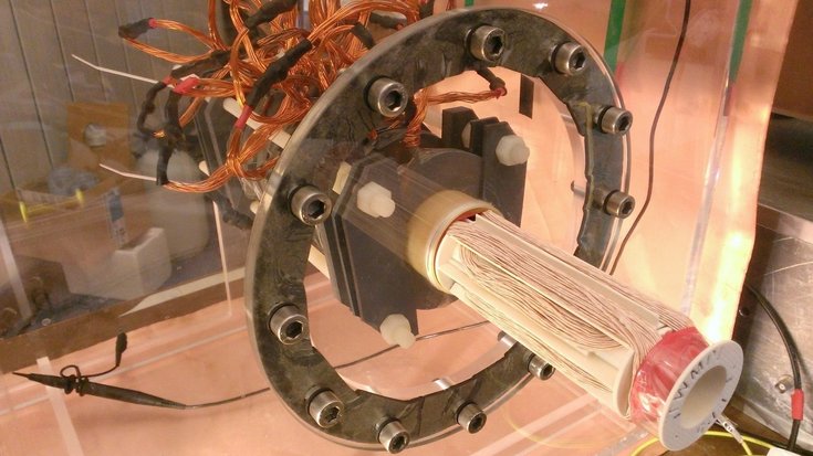 Das Bild zeigt den experimentellen Aufbau aus vielen Kabeln, einem Metallring und einer zylindrischen Röhre.