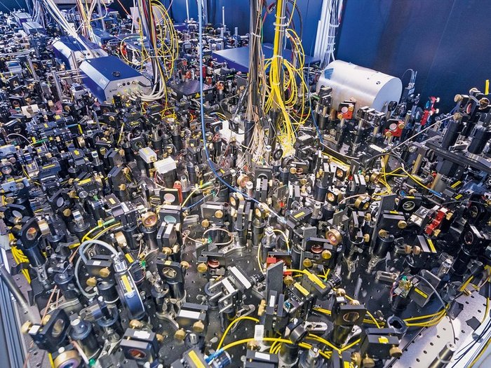 Experimenteller Aufbau Das Bild zeigt einen Teil des Experiments: Auf einem Labortisch sind unzählige optische Elemente, wie Spiegel und Strahlteiler, befestigt.