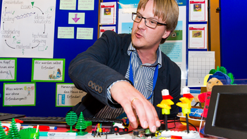 Ein Teilnehmer von Science on Stage sitzt an seinem Stand. Im Vordergrund stehen Legofiguren.