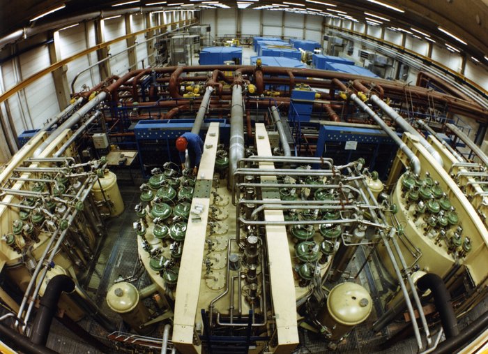 Mit einem Fischaugenobjektiv aufgenommenes Foto einer großen Halle, in der eine Kälteanlage mit verschiedenen zylinderförmigen Behältern und einer Vielzahl von Rohrleitungen aufgebaut ist.
