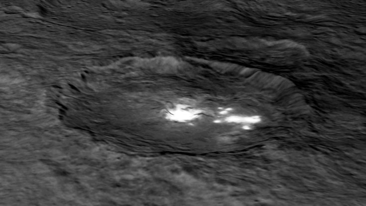Eine schräge Draufsicht auf einen Krater zeigt helle Flecken in dessen innerem Becken.