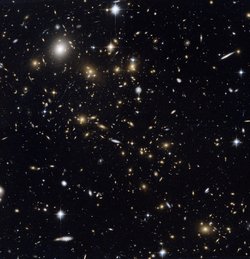 Ein Haufen Galaxien vor dem dunklen Hintergrund des Weltalls, auf dem Foto als leuchtende Flecken in unterschiedlichen Größen und Helligkeiten. Die Galaxien sind unterschiedlich verteilt, an einigen Stellen treten sie gehäuft auf, andere Stellen sind vergleichsweise leer.