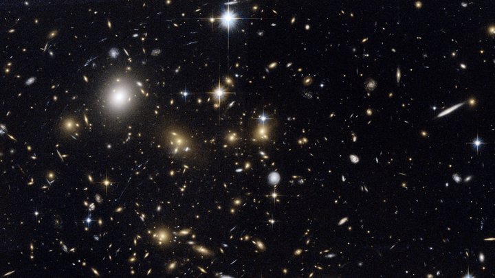 Ein Haufen Galaxien vor dem dunklen Hintergrund des Weltalls in unterschiedlichen Größen und Helligkeiten. 