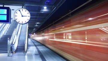 Foto eines Bahnsteigs, auf dem eine Uhr sowie ein einfahrender Zug zu sehen sind.