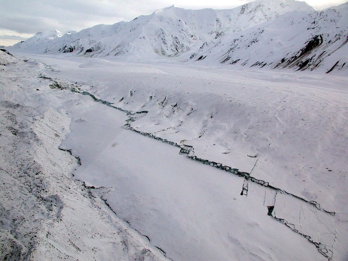 Spur des Bebens Eingeschneites Gebirge im Hintergrund. Davor Tal, ebenfalls weiß vom Schnee. Mitten im Schnee frische dunkle Bruchkanten.
