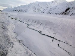 Eingeschneites Gebirge im Hintergrund. Davor Tal, ebenfalls weiß vom Schnee. Mitten im Schnee frische dunkle Bruchkanten.