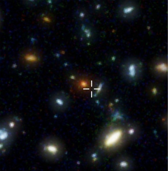 Galaxie HDF 850.1 Teleskopaufnahme mehrerer Galaxien und Galaxienhaufen, die in verschiedenen Farben leuchten. Eine Stelle des Bildes ist mit einem Kreuz markiert.