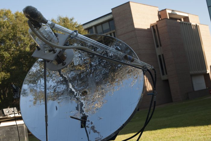 Die Anlage steht auf einer Wiese, sie besteht aus einer Parabolschüssel, die Sonnenlicht auf einen durchsichtigen Behälter in ihrem Brennpunkt fokussiert.