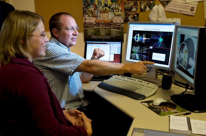 Rekonstruktion von Daten des LHCb-Experiments Ein Mann und eine Frau sitzen vor mehreren Computermonitoren und diskutieren dort angezeigte Daten.