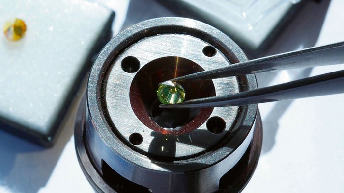 Diamantstempelzelle Die Aufnahme zeigt eine runde Fassung, in die mit einer Pinzette ein kleiner Diamant platziert wird.