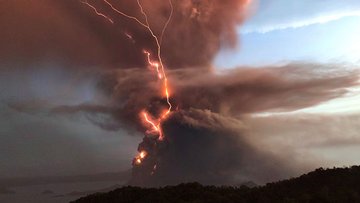Über einem ausbrechenden Vulkan ist ein Blitz zu sehen, der scheinbar brennt