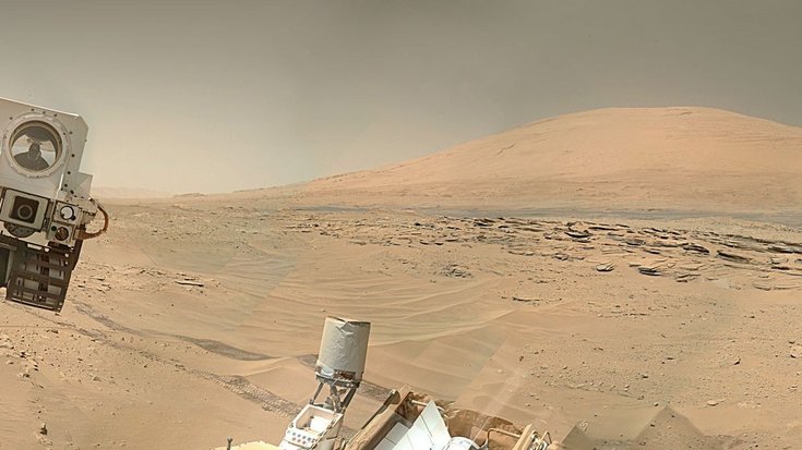 Marslandschaft mit Berg, im Vordergrund ein Teil des Rovers Curiosity.