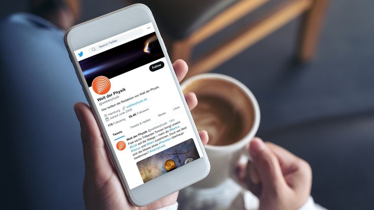 Das Foto zeigt eine Frau, die ein Smartphone in der Hand hält. Auf dem Display ist die Twitter-Seite von Welt der Physik zu sehen.