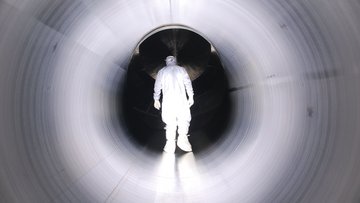 Ein Mann in einem weißen Schutzanzug läuft durch eine weiße Röhre auf ein dunkles Ende des Tunnels zu.