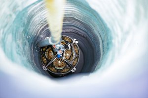 Ein technisches Gerät wird an einem Seil in ein Bohrloch im Eis hinuntergelassen.