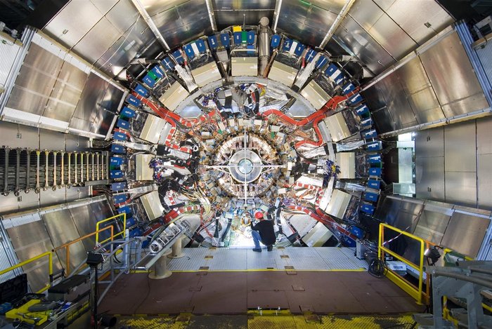 Der innere Spurdetektor von ATLAS Ein Mensch hockt vor einer sehr großen, zylinderförmigen technischen Apparatur mit einer Vielzahl von Einzelkomponenten, Kabeln und so weiter.